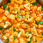 A pot of chickpea and cauliflower curry garnished with herbs.