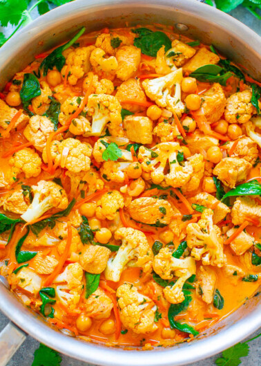 A pot of chickpea and cauliflower curry garnished with herbs.