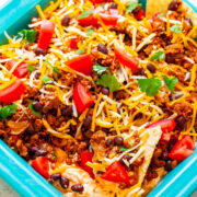 A colorful taco salad with ground beef, beans, shredded cheese, tomatoes, and cilantro in a blue dish, served with tortilla chips.