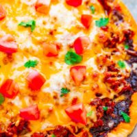 A freshly baked pizza with melted cheese, tomato pieces, and cilantro garnish on top.