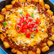 A skillet with cheesy ground beef and tater tots topped with fresh tomatoes and cilantro.