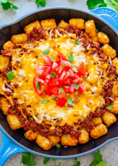 A skillet with cheesy ground beef and tater tots topped with fresh tomatoes and cilantro.