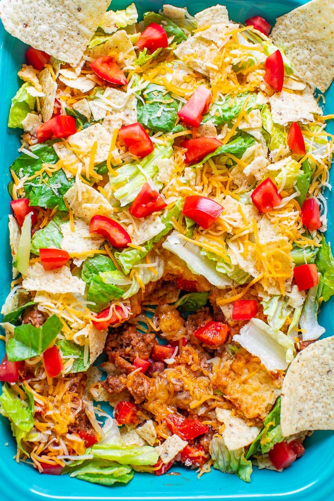 A plate of nachos topped with melted cheese, lettuce, tomatoes, and ground meat.