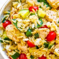 A bowl of rice mixed with diced chicken, zucchini, cherry tomatoes, and herbs.