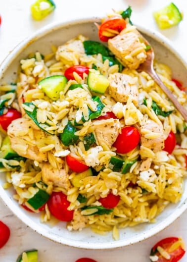 A bowl of chicken and orzo salad with cherry tomatoes, zucchini, and herbs.