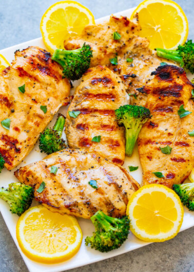 Grilled chicken breasts with broccoli garnish and lemon slices on a plate.
