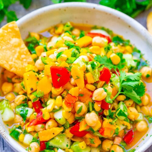 A bowl of mango, corn chickpea salad with a tortilla chip sticking out.