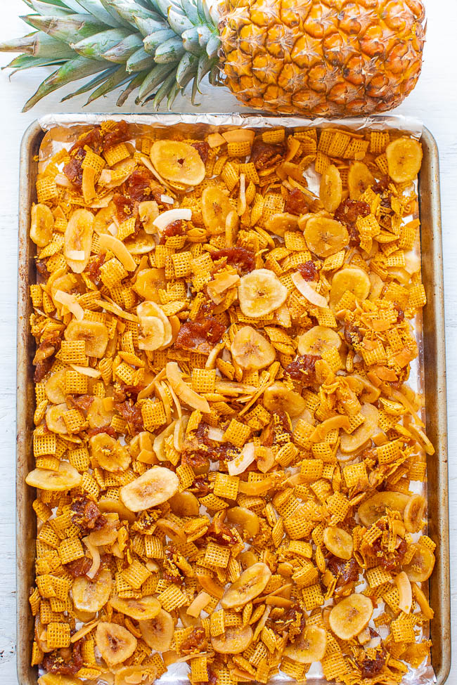 overhead view of sweet chex mix on a baking tray. A pineapple rests at the top 
