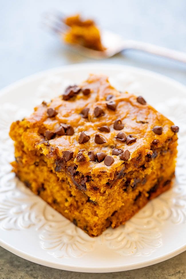 slice of pumpkin chocolate chip cake on a white plate. A fork with a bite of cake on it rests in the background. 