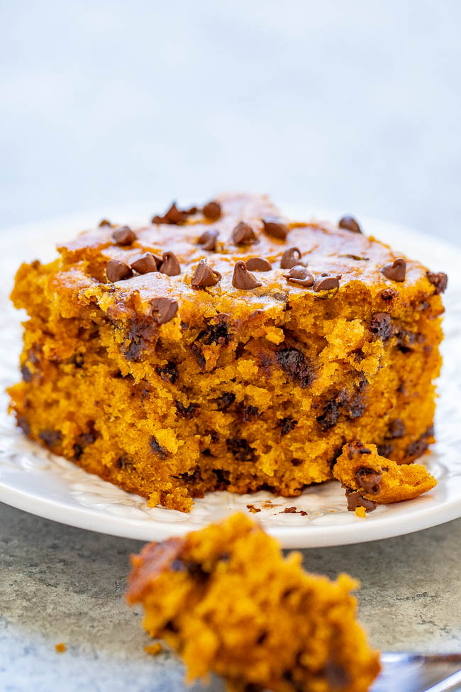 slice of pumpkin chocolate chip cake on a white plate. A fork with a bite of cake on it rests in the foreground. 