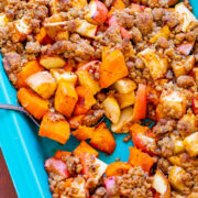 A spoon stuck into a baking dish with sweet potatoes and apple casserole.