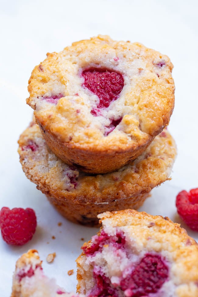 Stack of raspberry muffins with one broken in half, showing the fruit filling.
