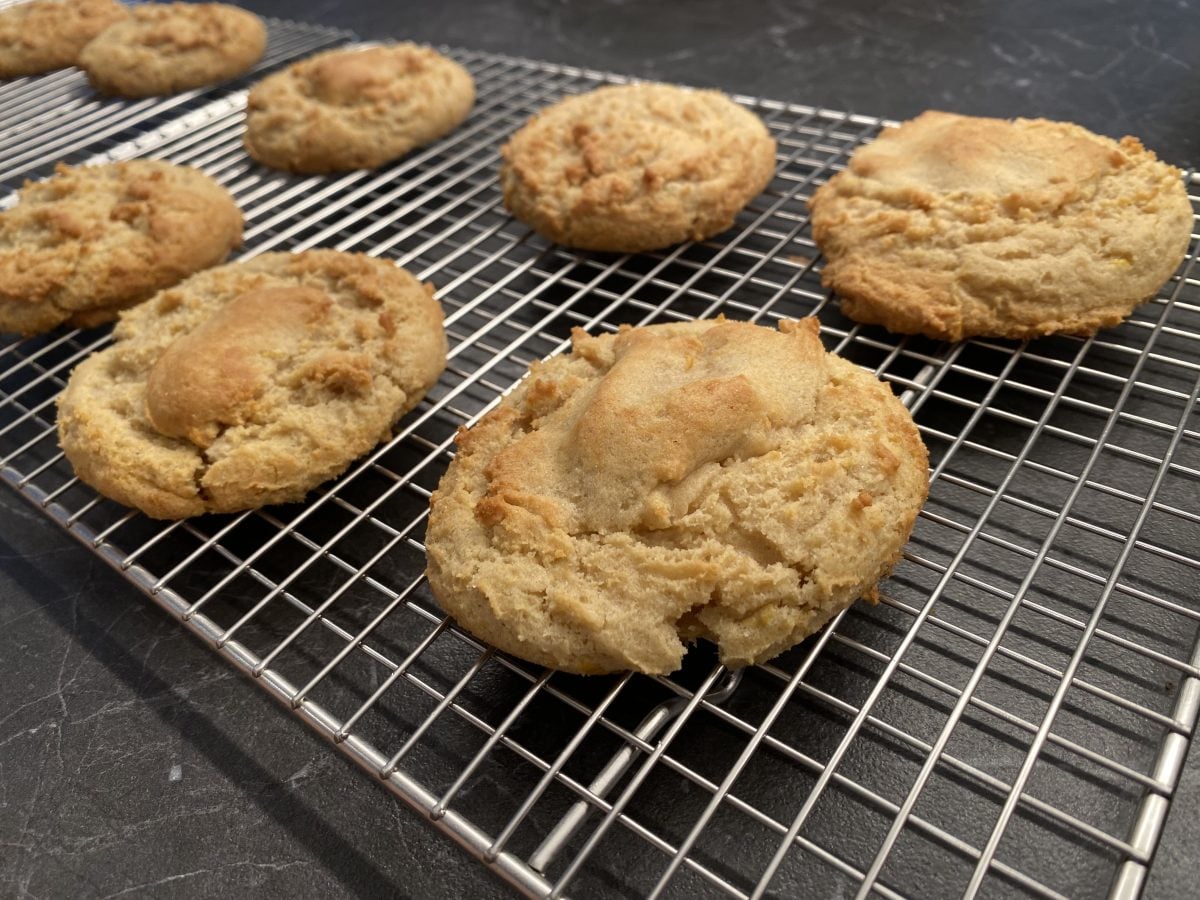 Seven golden brown cookies cooling on a metal wire rack placed on a dark countertop.