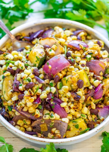 A fresh corn salad with red onion, herbs, and beans in a serving bowl.