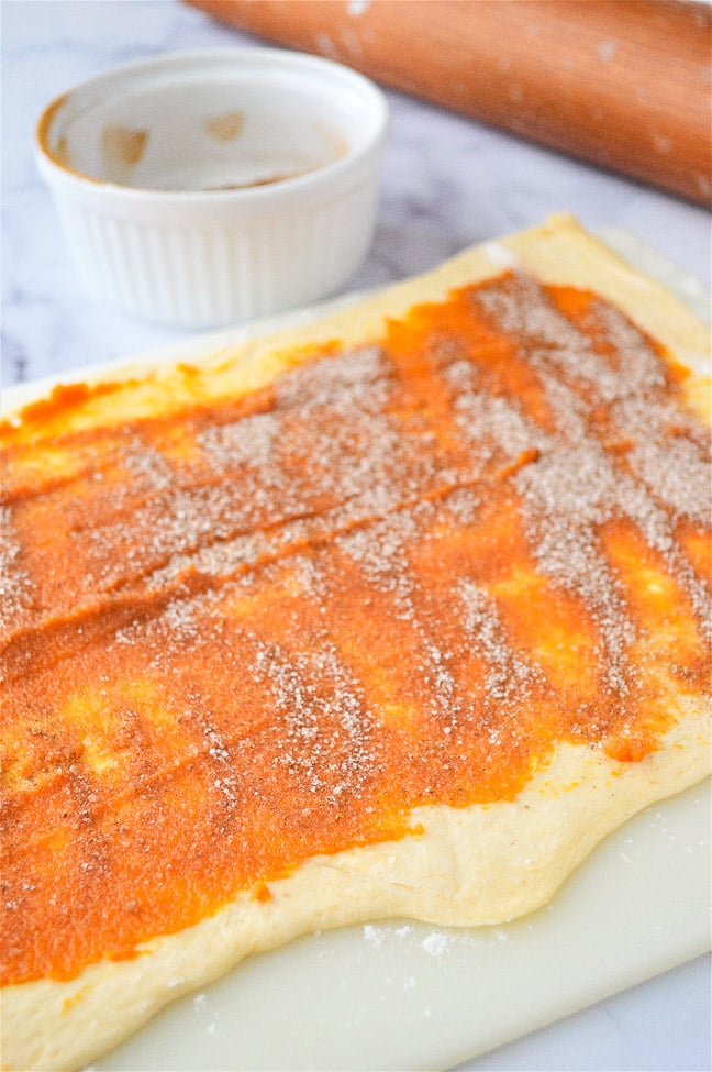 Rolled dough spread with tomato sauce and sprinkled with cheese, ready for cooking.