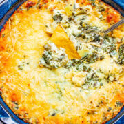 Baked Spinach Artichoke Dip in a bowl with a spoon sticking out.
