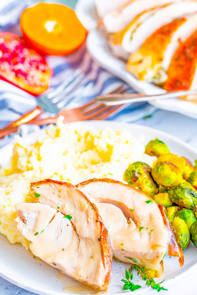 Two slices of oven roasted Thanksgiving turkey on a plate with mashed potatoes and Brussels sprouts. 