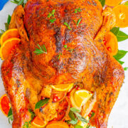 Roasted chicken garnished with slices of orange and herbs on a serving platter.