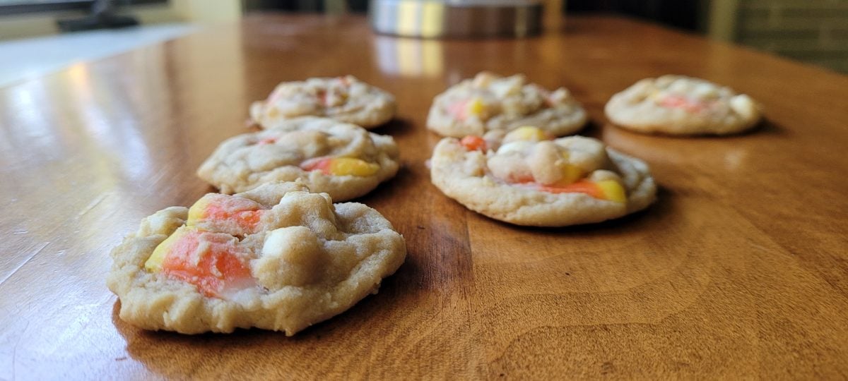Six cookies with candy corn pieces arranged on a wooden table.