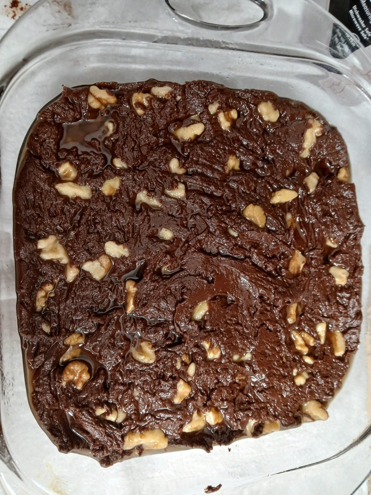 A glass baking dish filled with unbaked chocolate brownie batter topped with walnut pieces.