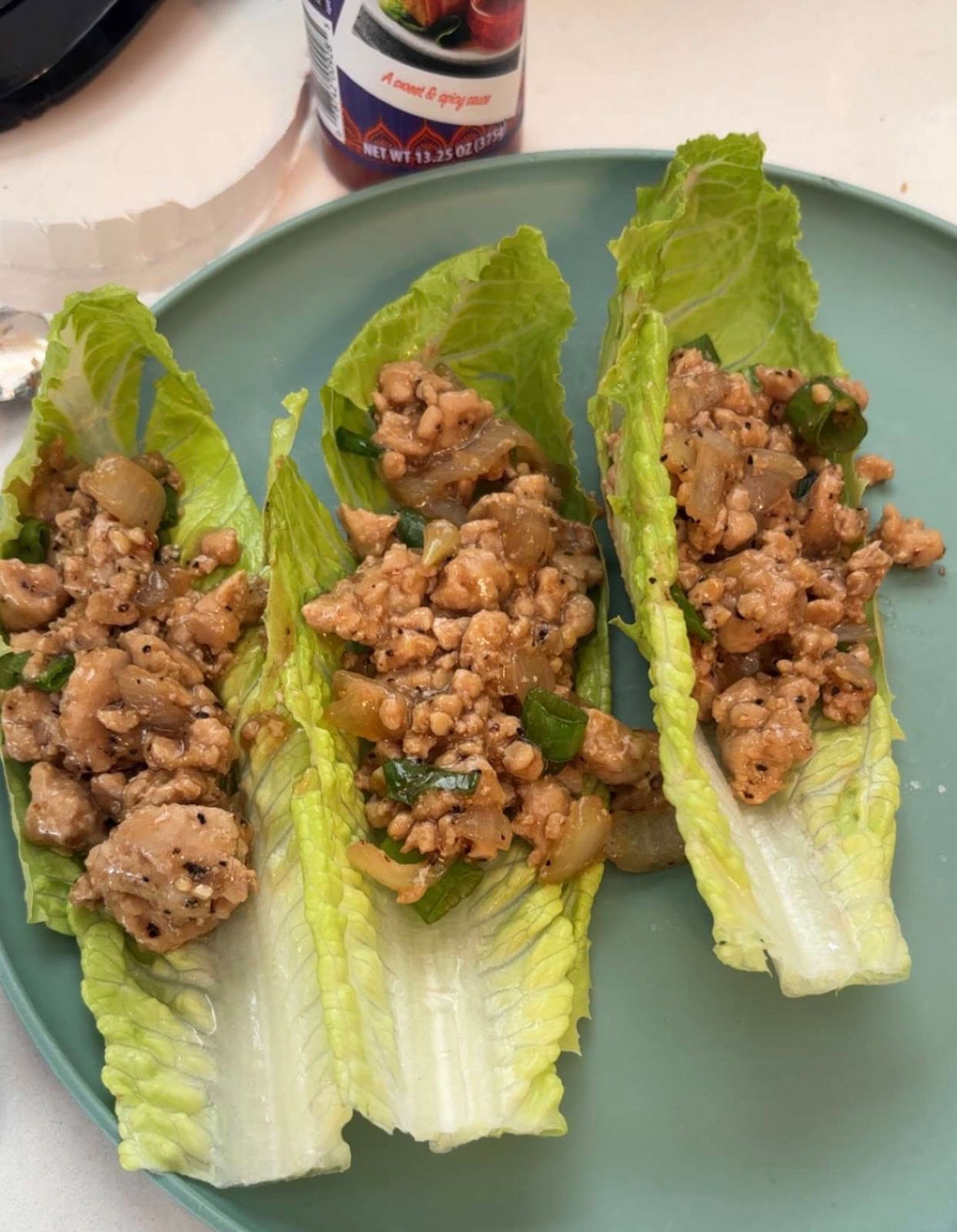 Three romaine lettuce leaves filled with cooked ground meat, chopped vegetables, and sauce, arranged on a green plate.
