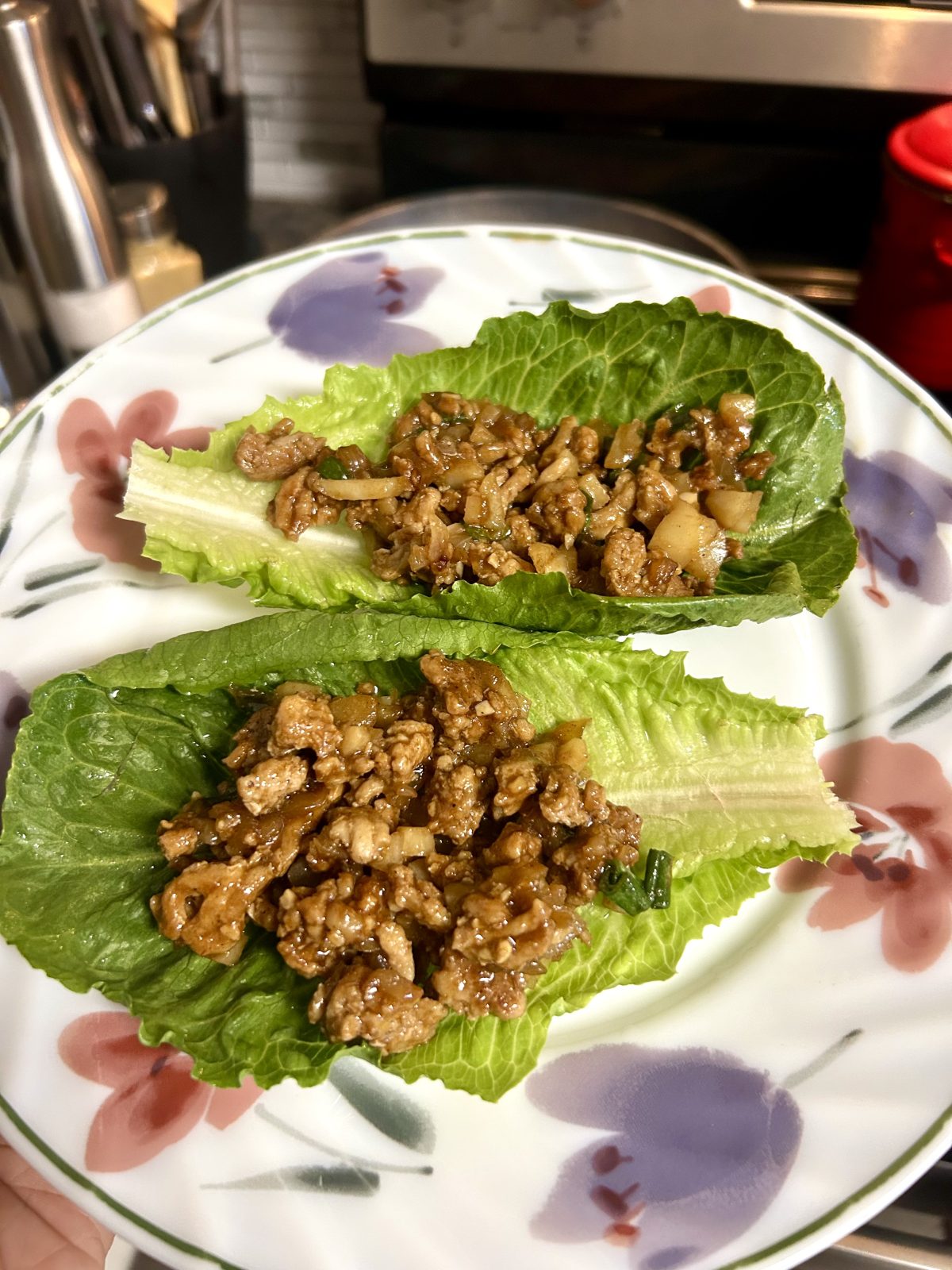 Two lettuce leaves filled with cooked ground meat and diced vegetables on a decorative plate.