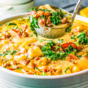 Loaded Zuppa Toscana in a pot, a ladle lifting a scoop.