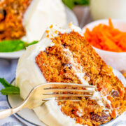 A slice of layered spiced carrot cake with cream cheese frosting with a fork digging in.