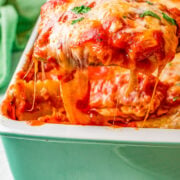 A slice of lasagna with melted cheese being lifted from the tray.