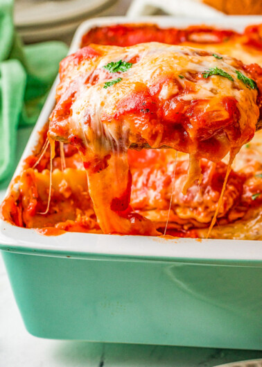 A slice of lasagna with melted cheese being lifted from the tray.