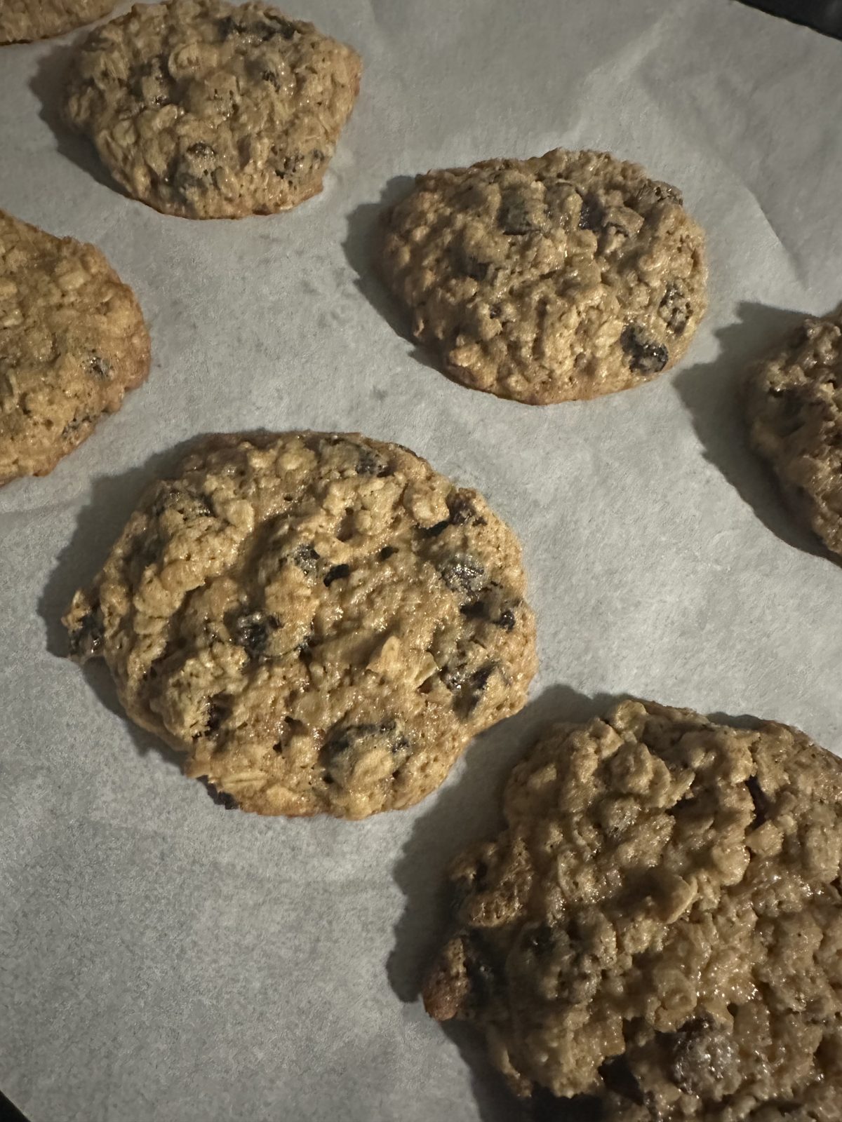 Six oatmeal raisin cookies cooling on parchment paper.