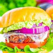A black bean burger with lettuce, tomato, cheese, red onion, and guacamole.