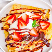 A plate of basic crepes with peanut butter, chocolate sauce, strawberries, and whipped cream.