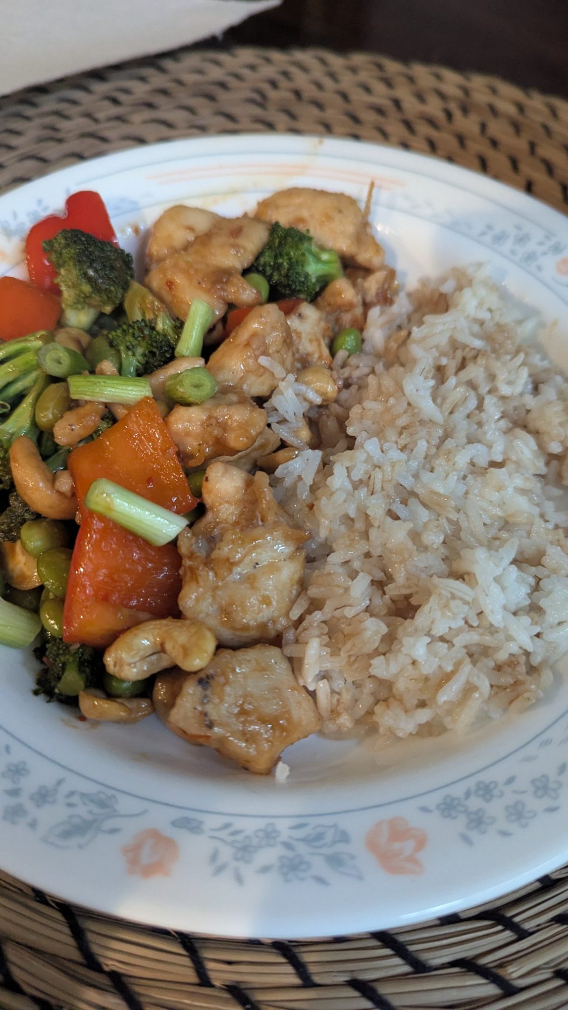 A plate of stir-fried chicken with broccoli, red bell peppers, green beans, and cashews served alongside steamed white rice.