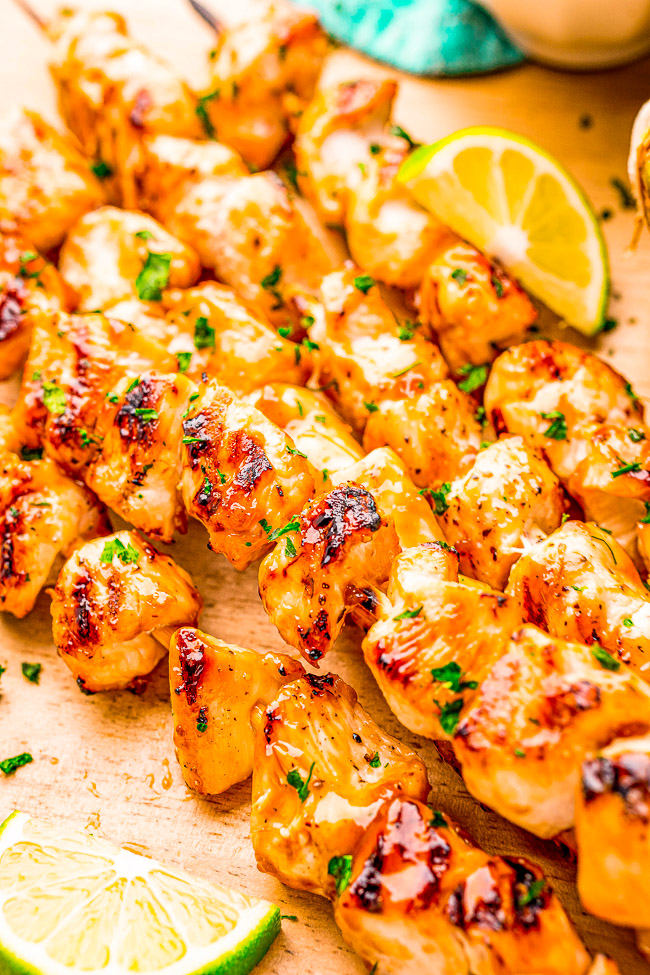Grilled chicken skewers garnished with parsley and lemon slices on a wooden board.