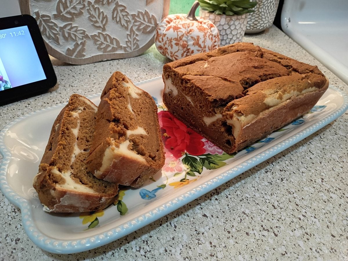 Sliced loaf of marble bread with cream cheese swirls on a floral serving tray, placed on a speckled kitchen countertop.