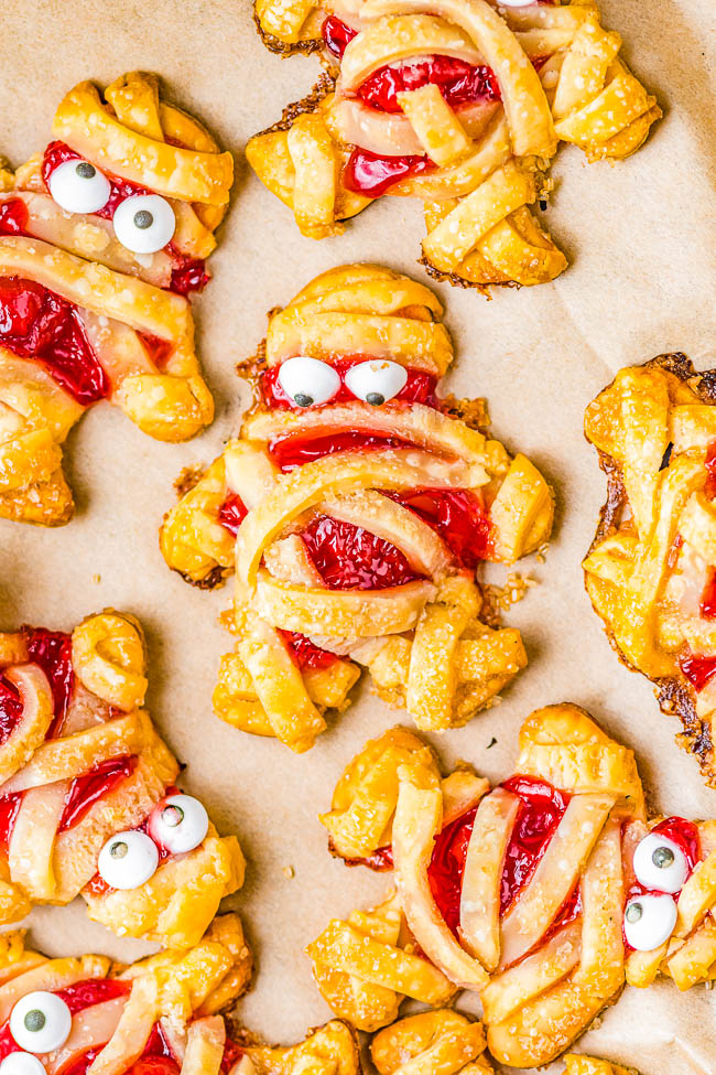 Mummy Hand Pies - A FUN and EASY Halloween treat that kids and adults alike both love! Buttery flakey pie crust with tangy-sweet cherry pie filling give great flavor to these festive and whimsical little goodies! Use store bought pie crust to save time and they're ready in 45 minutes. These little mummies will be the hit of your Halloween party!
