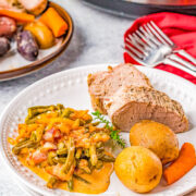 Slow Cooker Cheesy Green Bean Casserole on a plate with pork, potatoes, and carrots.