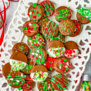 Chocolate covered Oreos decorated with Christmas sprinkles on a white platter.