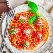 Homemade Spaghetti and Meatballs on a plate topped with fresh basil and Parmesan, a fork on the side.