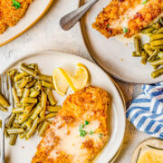 Air fryer breaded chicken breasts on two plates with green beans.
