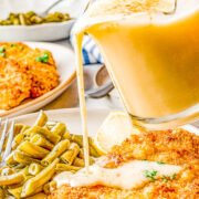 Lemon beurre blanc sauce being poured over crispy chicken on a plate with green beans.