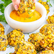 Baked Zucchini Corn Poppers on a plate, one being dipped into a yellow sauce.