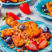 Air Fryer Cinnamon French Toast Sticks on a plate topped with chopped nuts, blueberries, and strawberries.