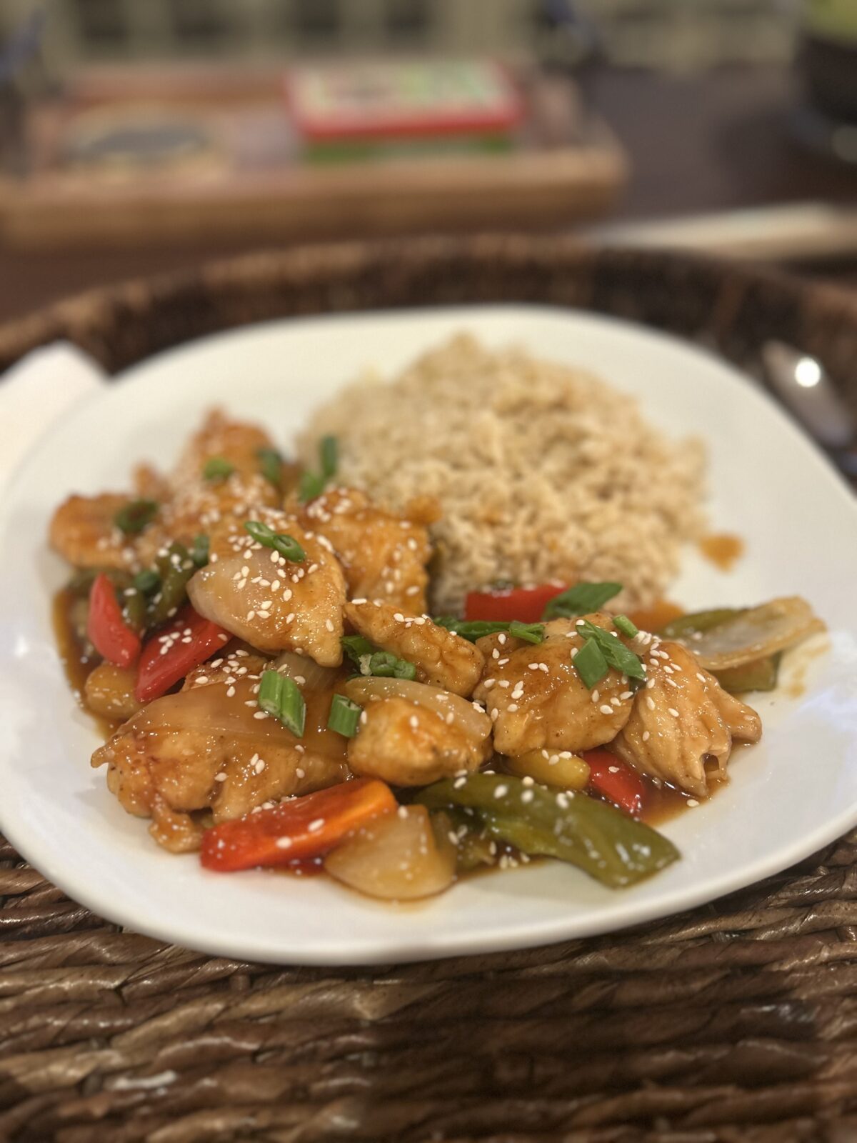 A plate of stir-fried chicken with bell peppers, onions, and sesame seeds next to a serving of brown rice.