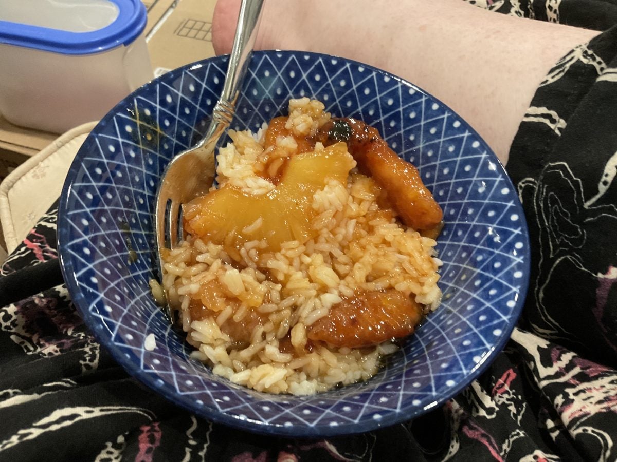A blue patterned bowl contains rice, pineapple, and pieces of glazed chicken with a fork resting inside.