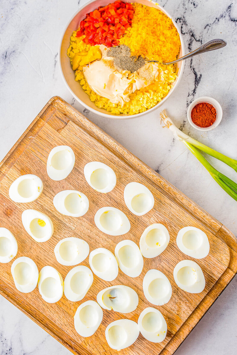 Hard boiled egg whites on a wooden cutting board next to a bowl of pimento cheese ingredients.