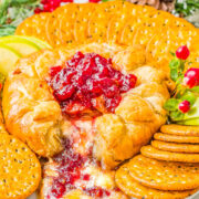 Baked Brie in Puff Pastry on a platter with a scoop missing surrounded by crackers and apple slices.