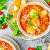 A bowl of pizza soup topped with garlic bread pieces.