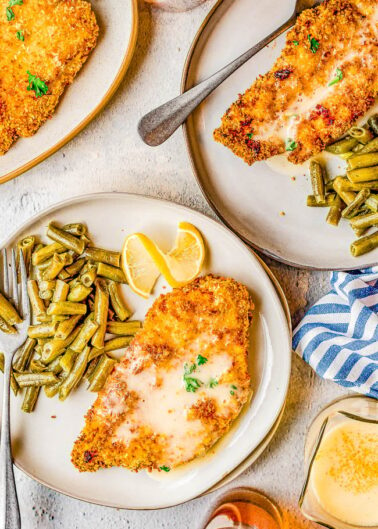 Breaded chicken cutlets served with green beans and lemon slices on a textured tabletop.